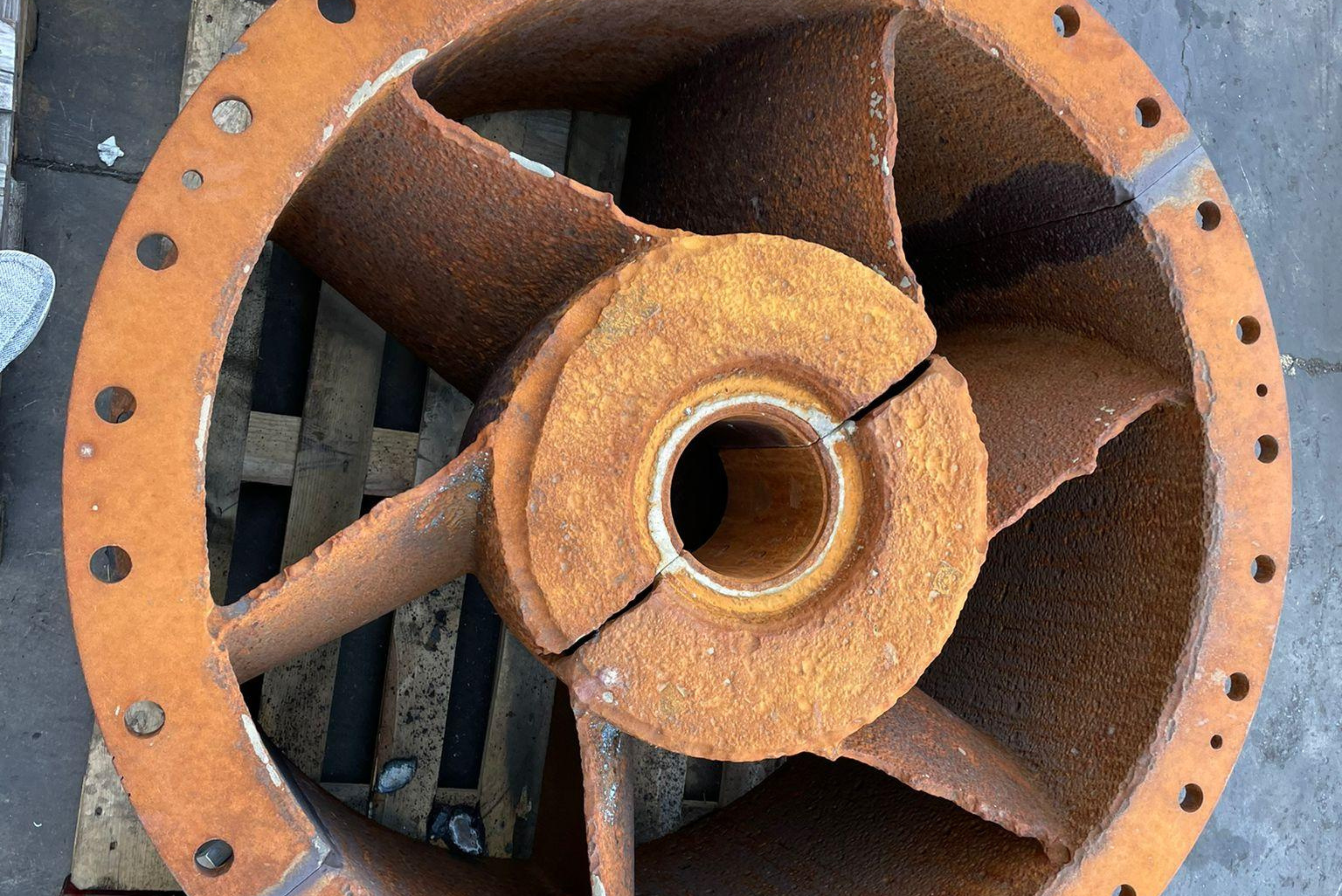 "Componente industrial de bomba ou turbina com pás metálicas avermelhadas enferrujadas, flanges de fixação com furos, núcleo central branco e estrutura de metal oxidado