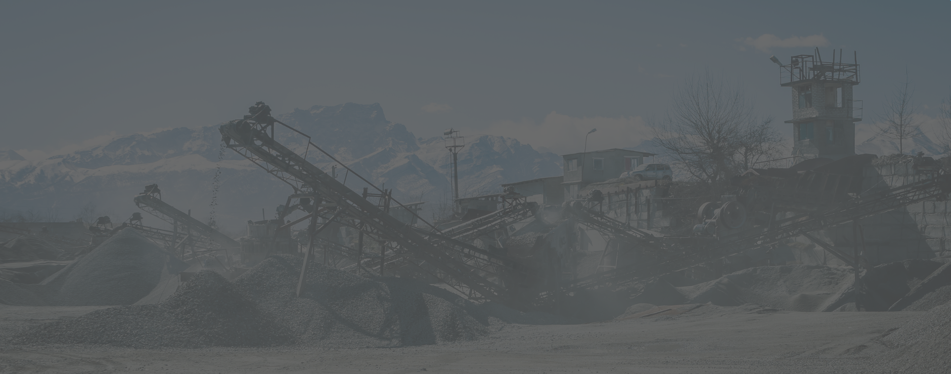 Uma paisagem industrial nebulosa e desbotada mostrando uma instalação de mineração ou pedreira com esteiras transportadoras inclinadas, montes de cascalho e estruturas de edifícios ao fundo contra montanhas