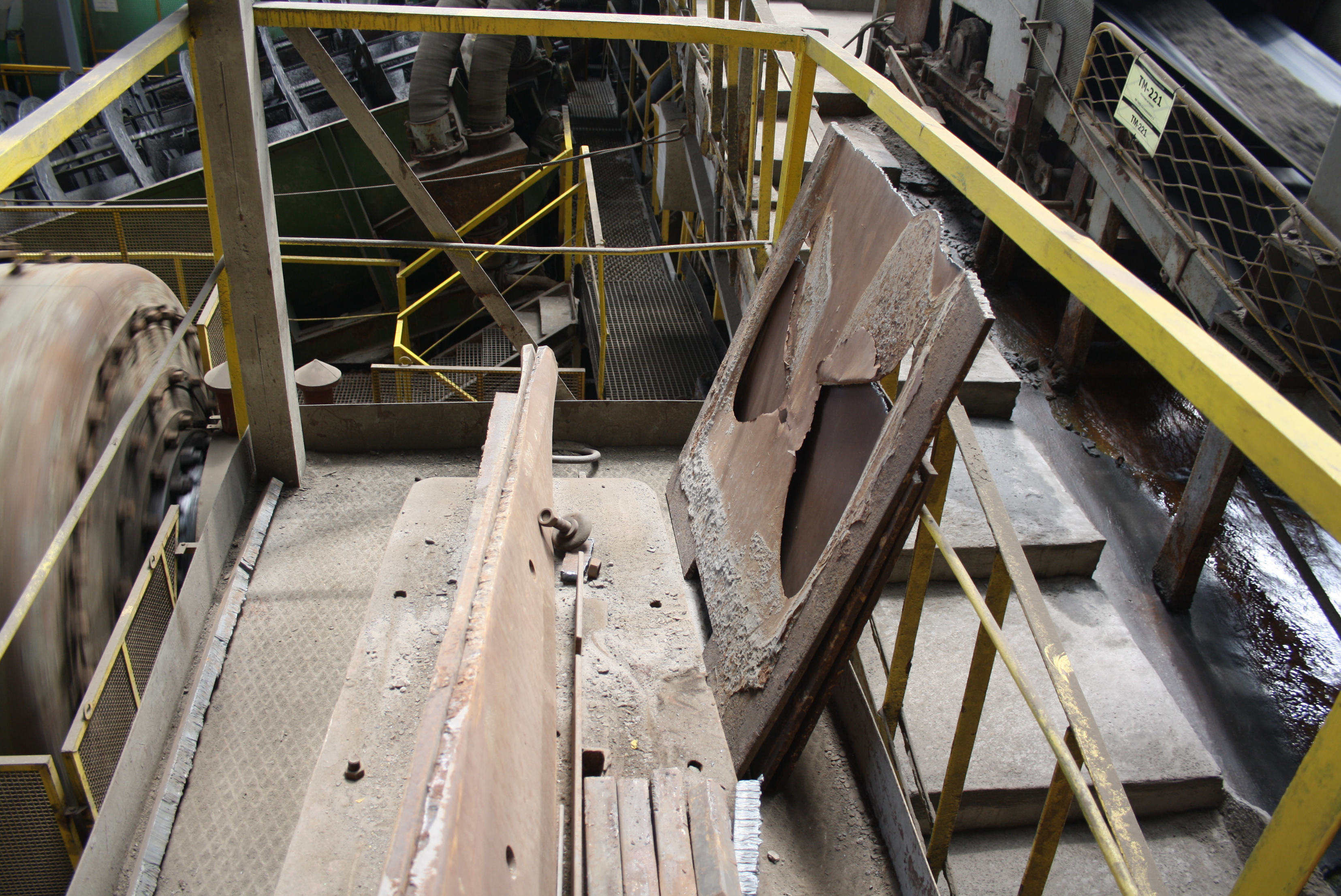 Vista aérea do interior de uma estrutura metálica industrial com railings amarelos, plataforma cinzenta com padrão antiderrapante, painéis de metal cinzento e equipamentos diversos instalados.