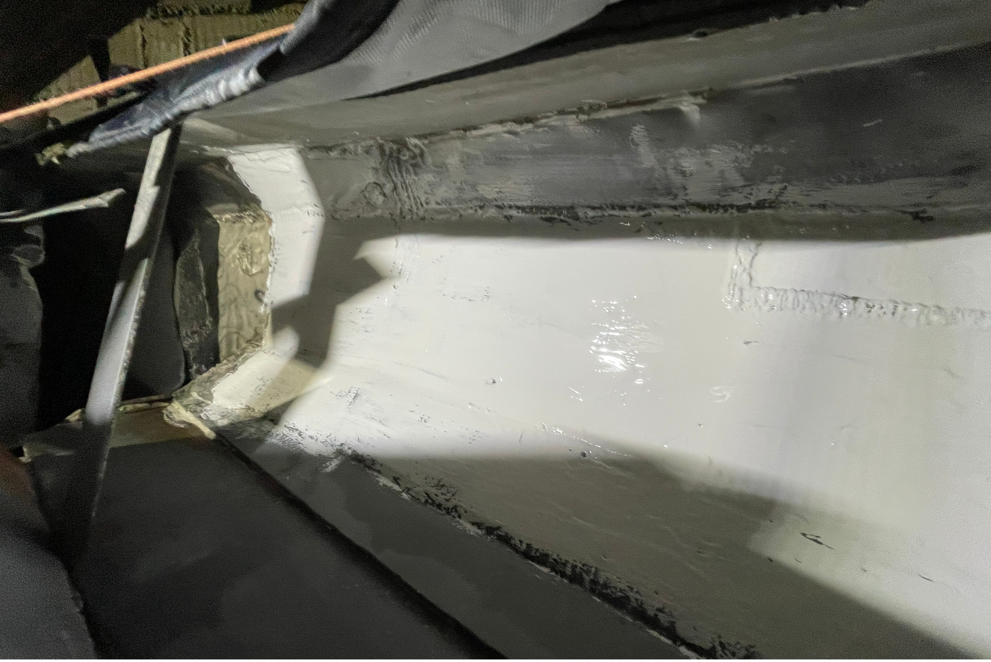 Detalhe de aplicação de revestimento branco em superfície metálica cinzenta, mostrando contraste entre área revestida e não revestida, com sombra de estrutura acima
