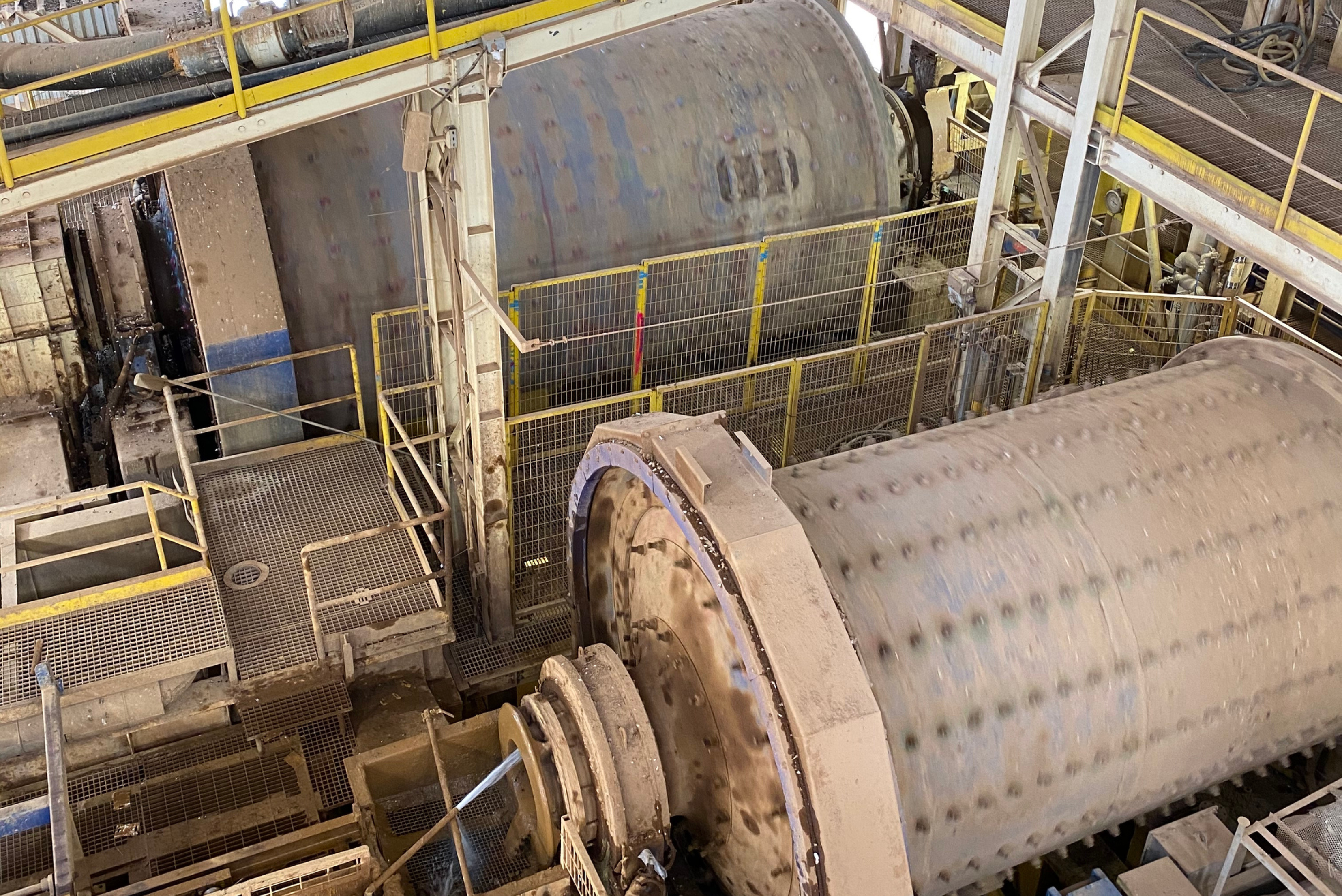 Vista superior de grandes cilindros industriais metálicos cinzentos com estruturas de suporte amarelas e brancas, mostrando equipamento de processamento em ambiente de fábrica com múltiplos componentes cilíndricos.