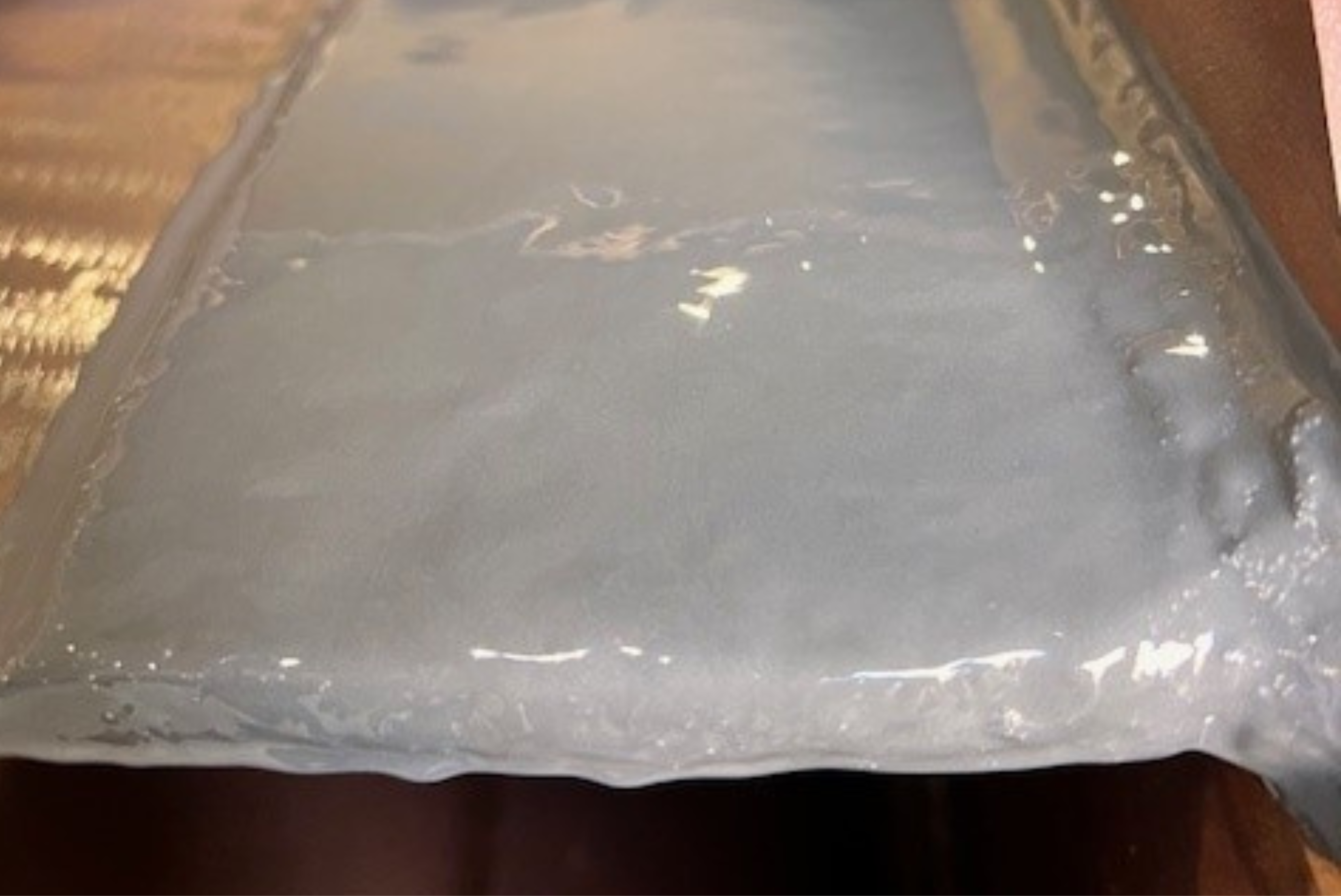 Uma superfície metálica ou estrutural revestida com uma camada espessa, lisa e brilhante de material de vedação ou resina cinza claro.