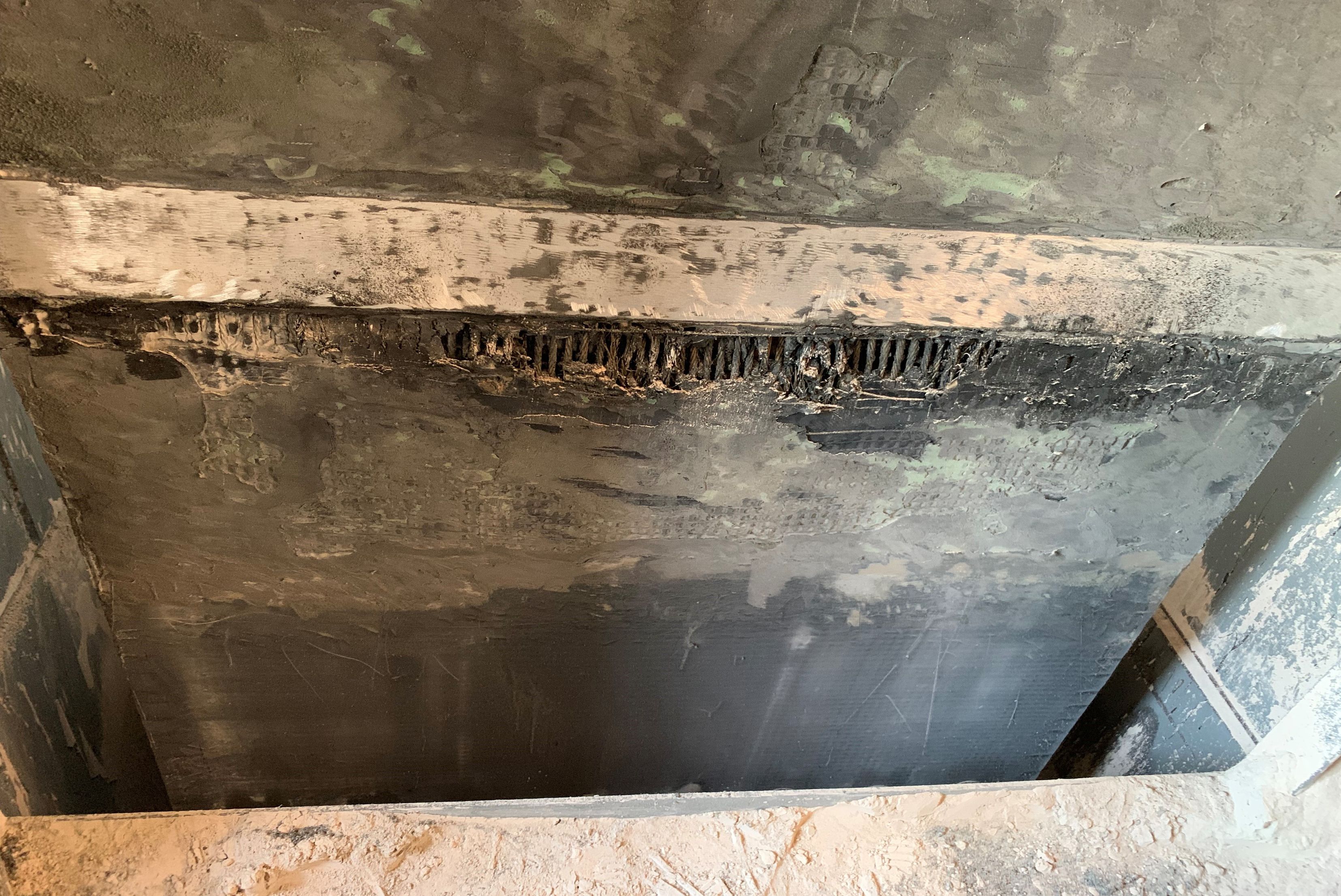 Detalhe de estrutura metálica enferrujada com parede interna escura, mostrando corrosão, depósitos de sujeira e desgaste do material, com abertura retangular visível.