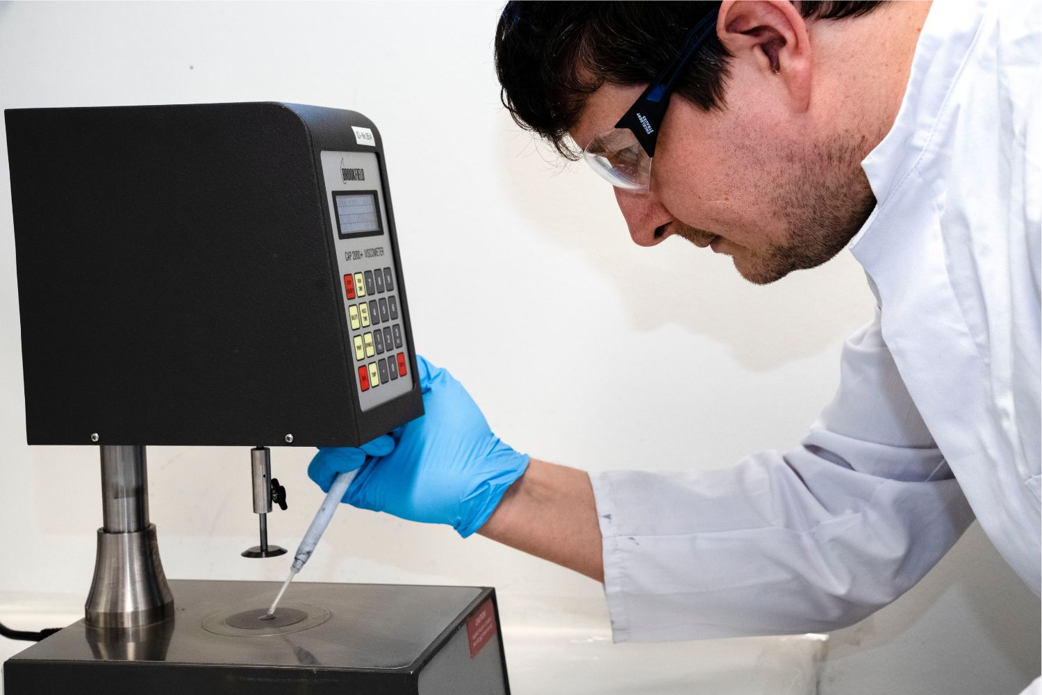 Um homem com bata branca coloca algo de uma pipeta numa superfície